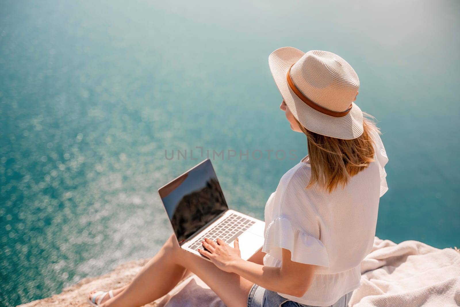 Freelance women sea working on the computer. Good looking middle aged woman typing on a laptop keyboard outdoors with a beautiful sea view. The concept of remote work. by Matiunina