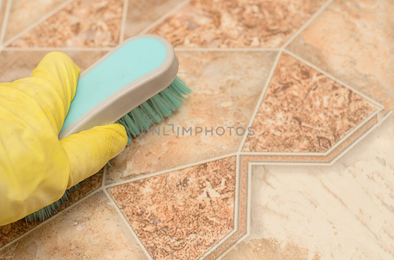 Man in yellow glove holds a brush for cleaning kitchen floor.