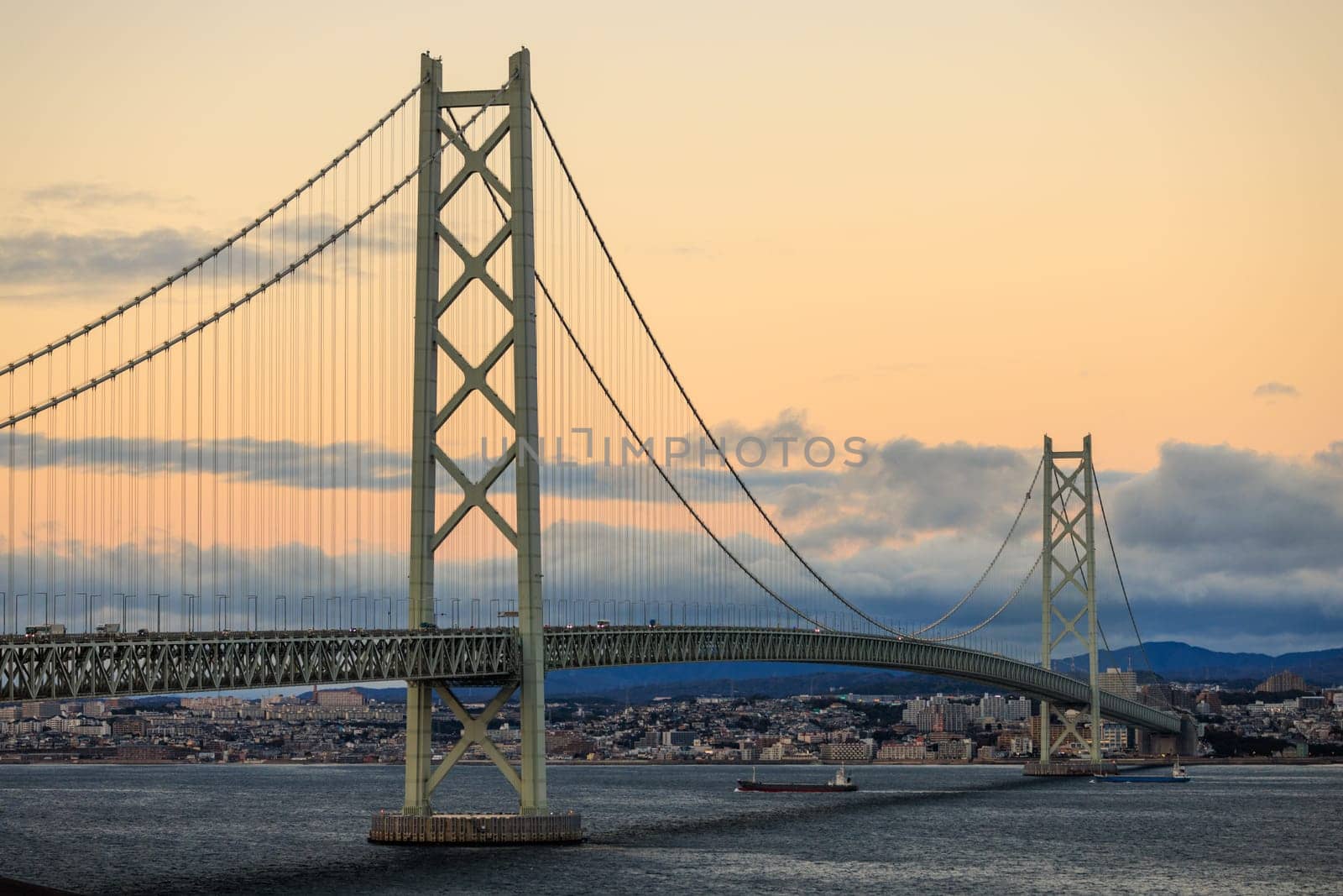 Orange Glow in Sky as Clouds Approach Suspension Bridge at Sunset. High quality photo