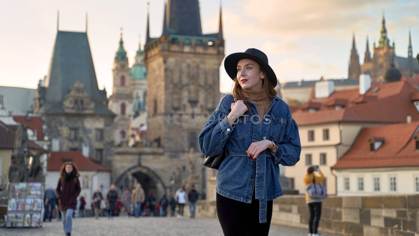 Female traveller tourist on the Charles Bridge in Prague, Czezh Repubic. Stylish beautiful young woman earing black hat. Elegant retro lady fine art portrait. by berezko