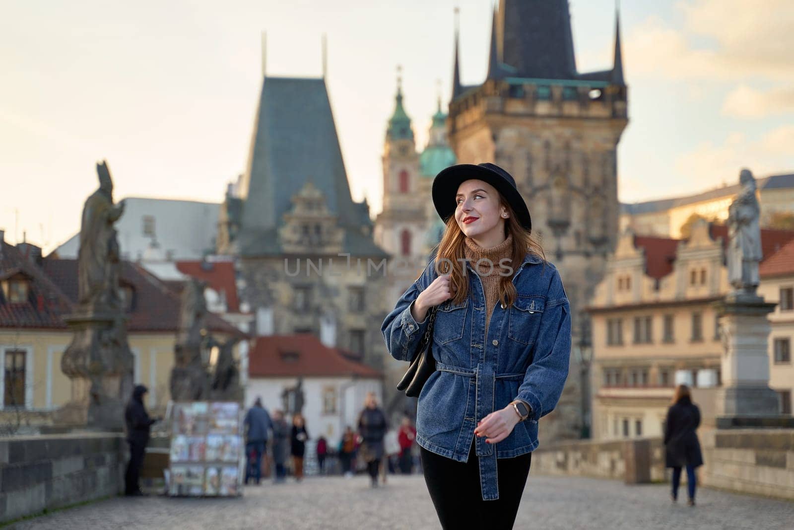 Female traveller tourist on the Charles Bridge in Prague, Czezh Repubic. Stylish beautiful young woman earing black hat. Elegant retro lady fine art portrait. by berezko