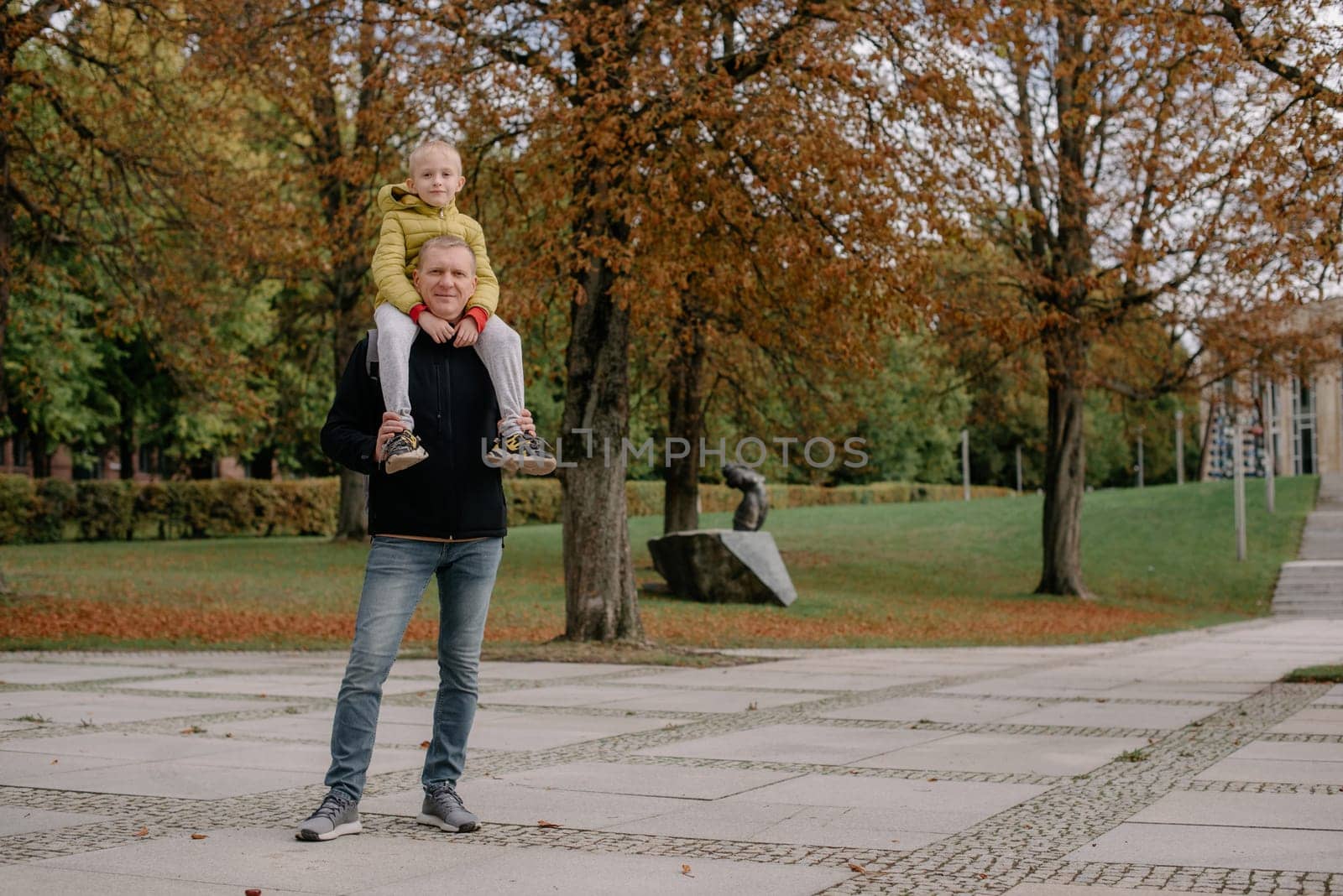 Dad holds on his son's shoulders. Beautiful family is spending time together outside. Dad and his little son are having fun on a roof terrace with view on a city. Sitting on father's shoulders and smiling.