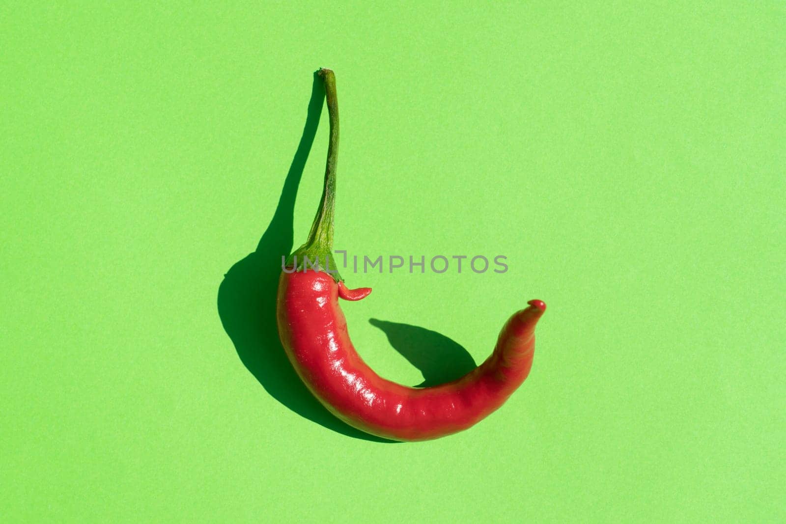 red hot pepper on a green background with a hard shadow. High quality photo