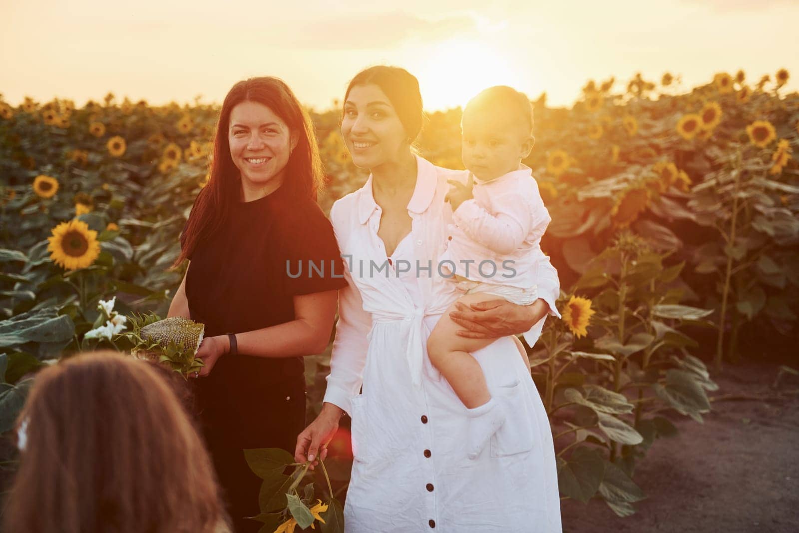 Young mother with her little son, daughter and female friend is outdoors in the agricultural field. Beautiful sunshine.