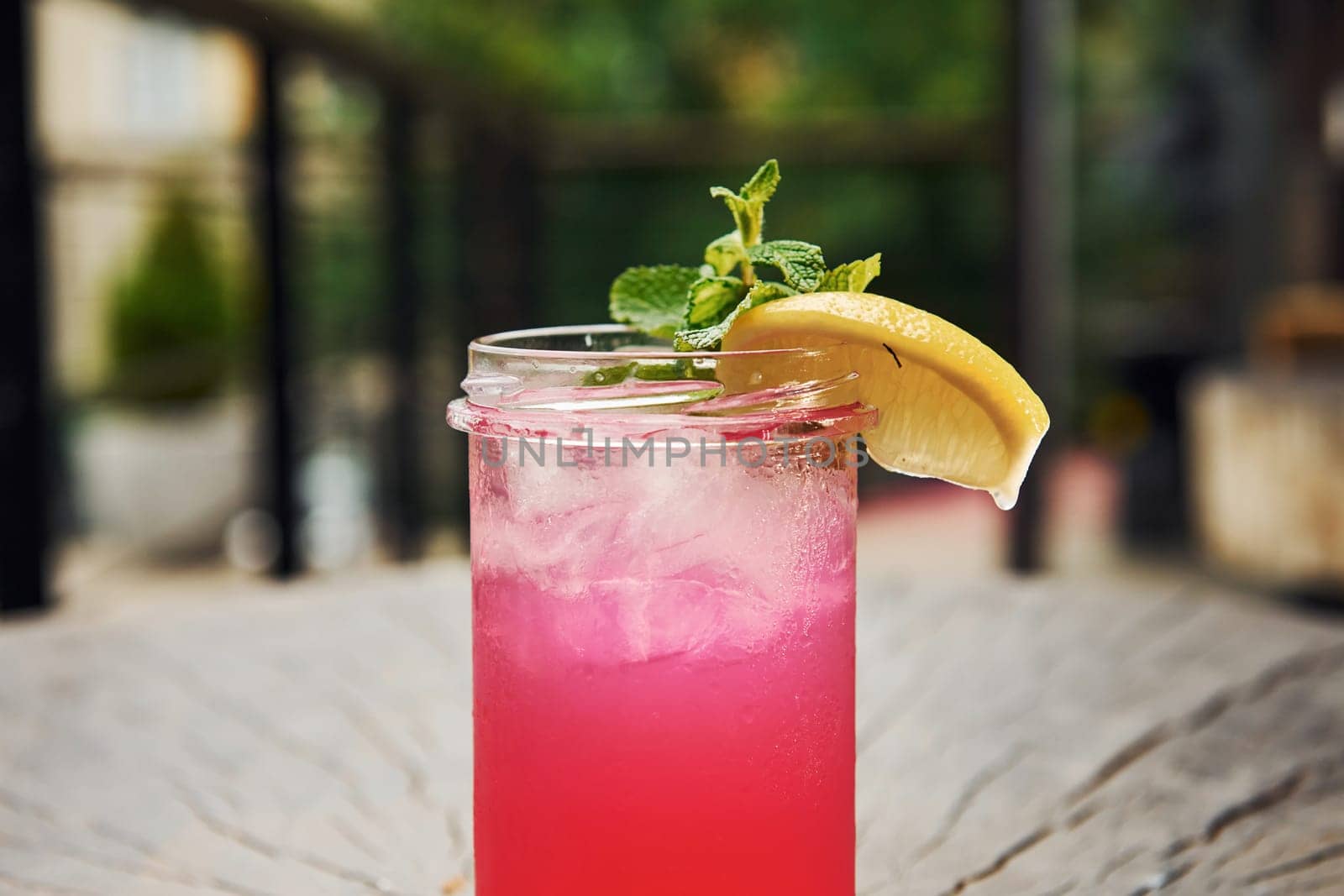 Pink colored liquid with lemon. Close up view of fresh summer alcoholic cocktail on the wooden table.