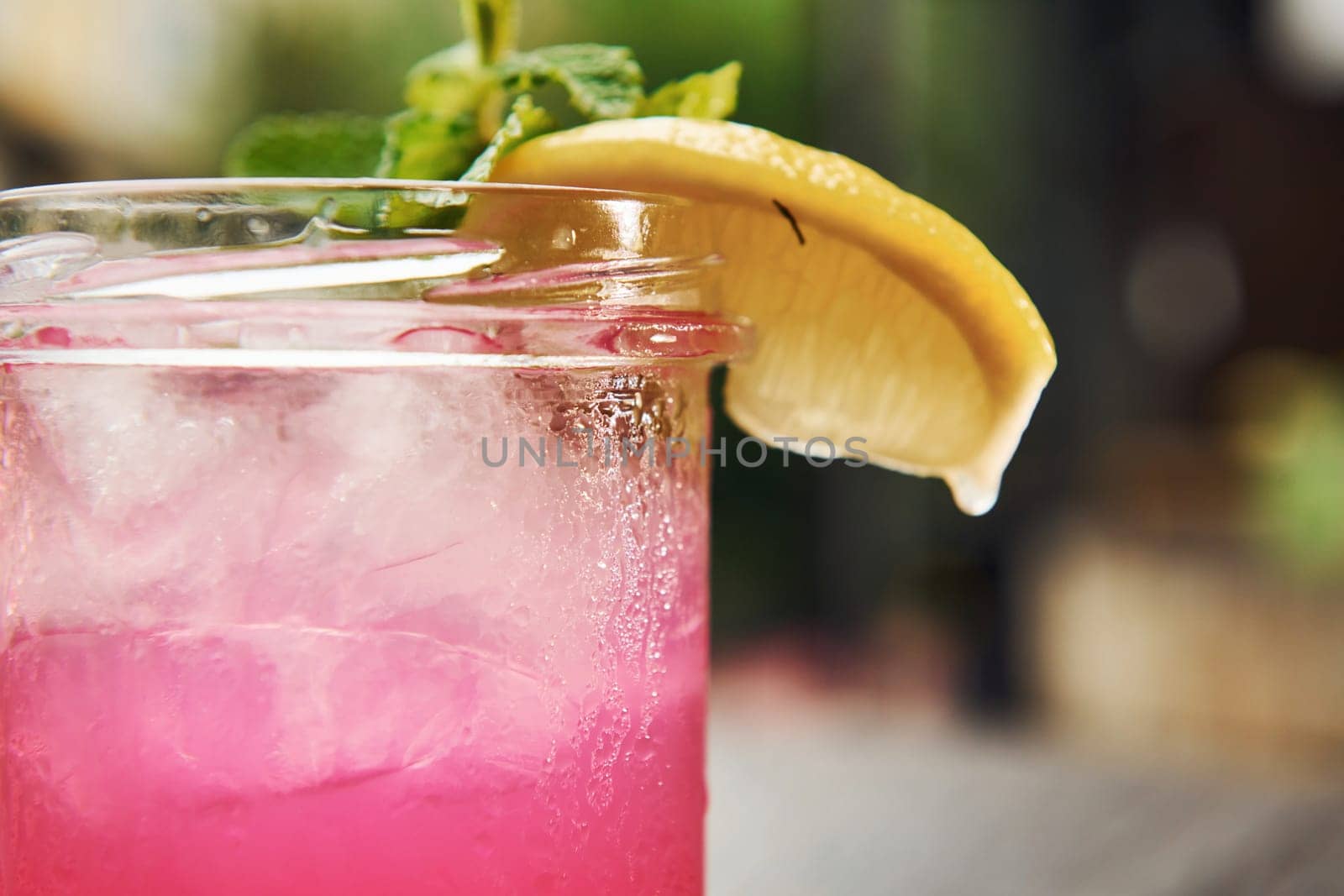 Pink colored liquid with lemon. Close up view of fresh summer alcoholic cocktail on the wooden table.