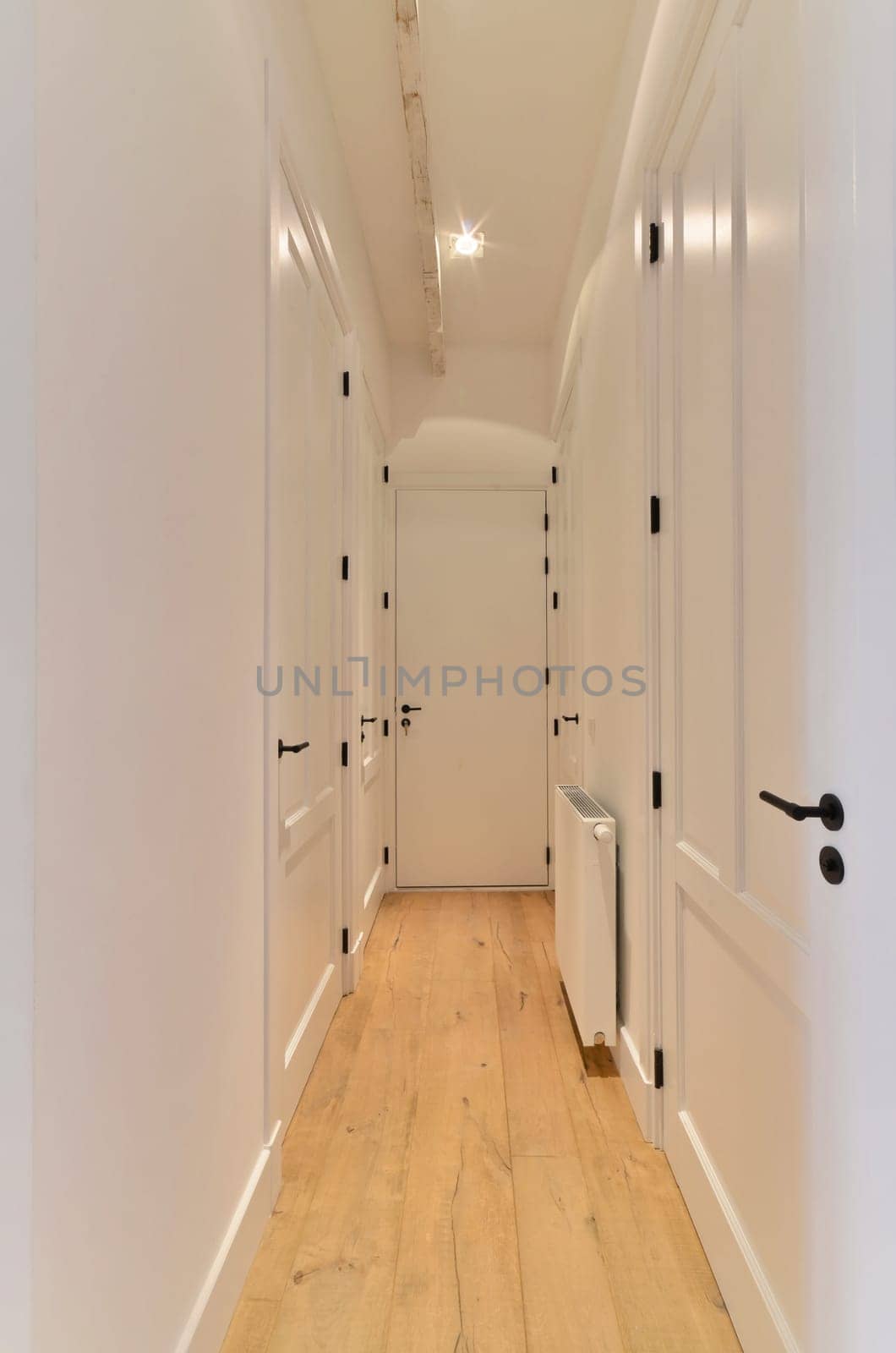 a hallway with white walls and wooden floors and doors by casamedia
