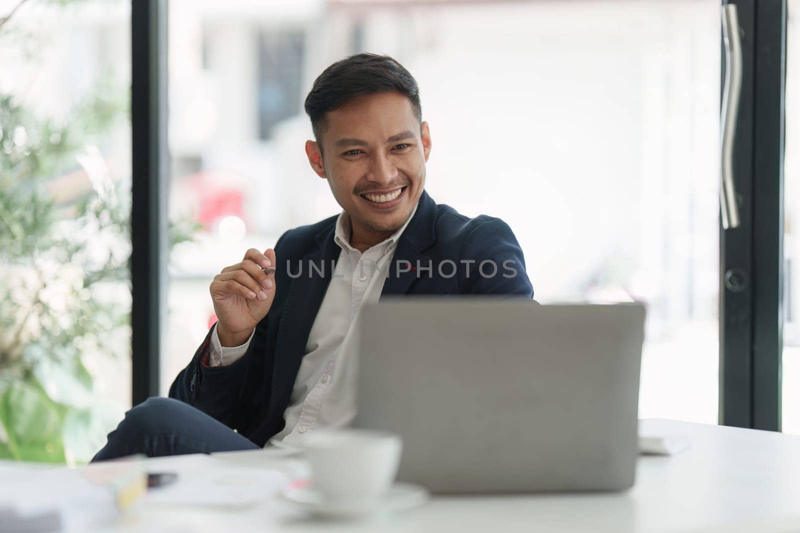 Smiling Asian Banker makes financial report and studies annual figures, analyzes profits. Accountant checks status of financial.