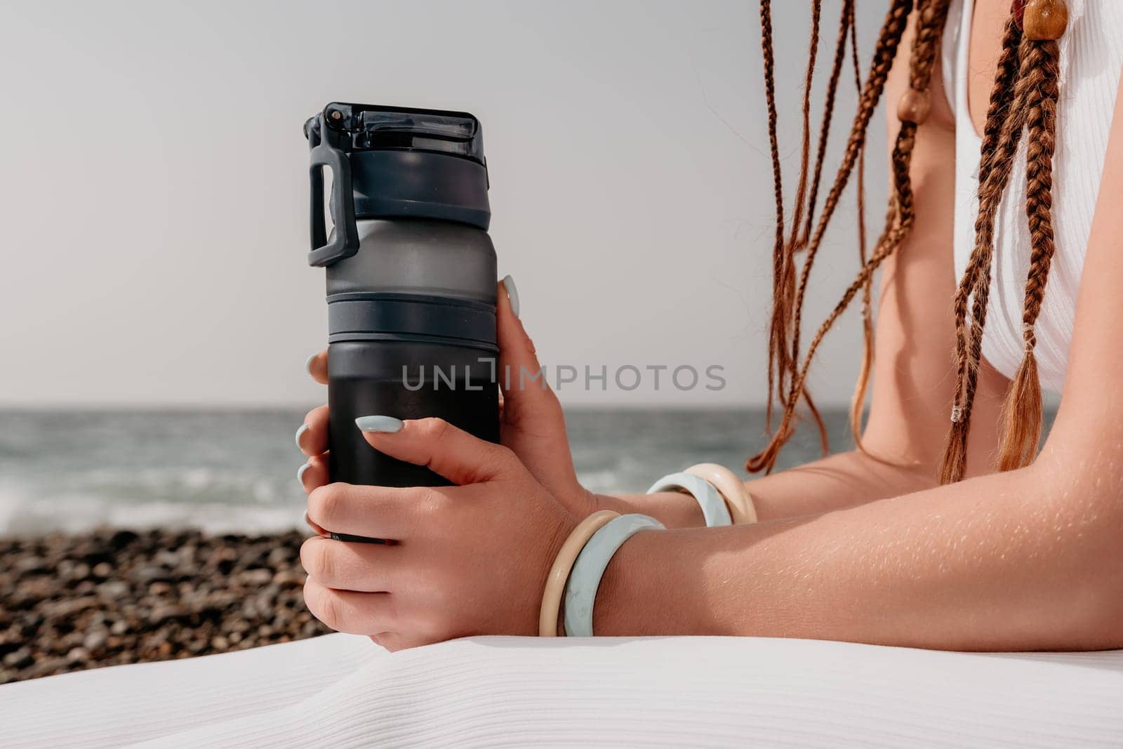 Woman yoga sea. Well looking middle aged woman with braids dreadlocks in white leggings and tops doing stretching pilates on yoga mat near sea. Female fitness yoga routine concept. Healthy lifestyle