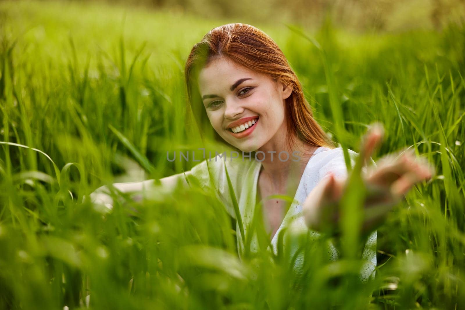 portrait of a broadly smiling woman sitting in tall grass and holding out her hands to the camera. High quality photo