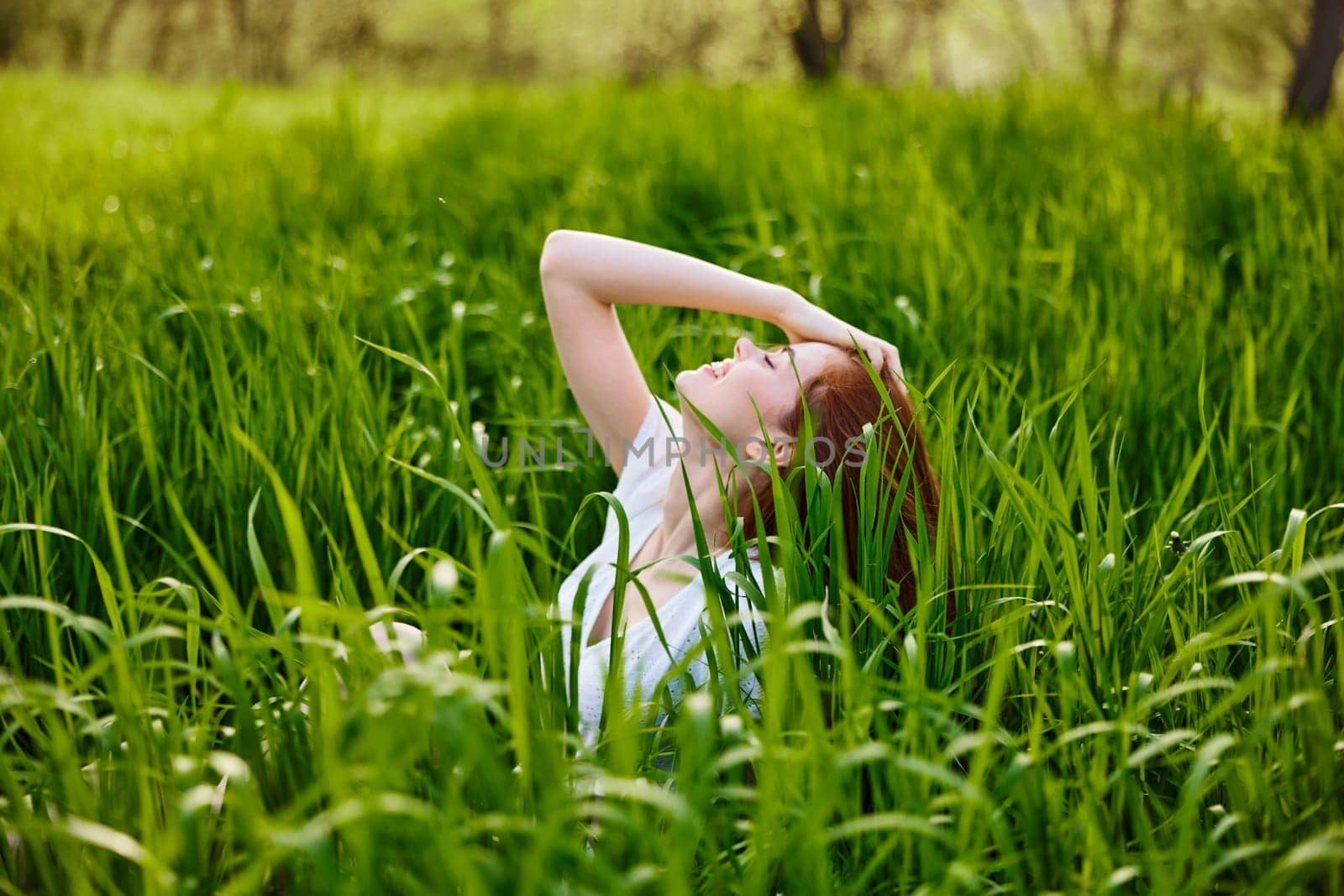 cute woman with red hair sits in tall green grass with her hand on her head by Vichizh