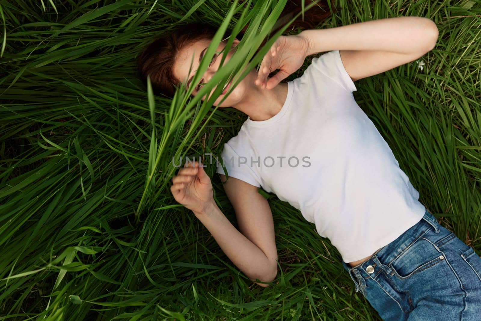happy woman lies in tall grass covering her face with leaves by Vichizh