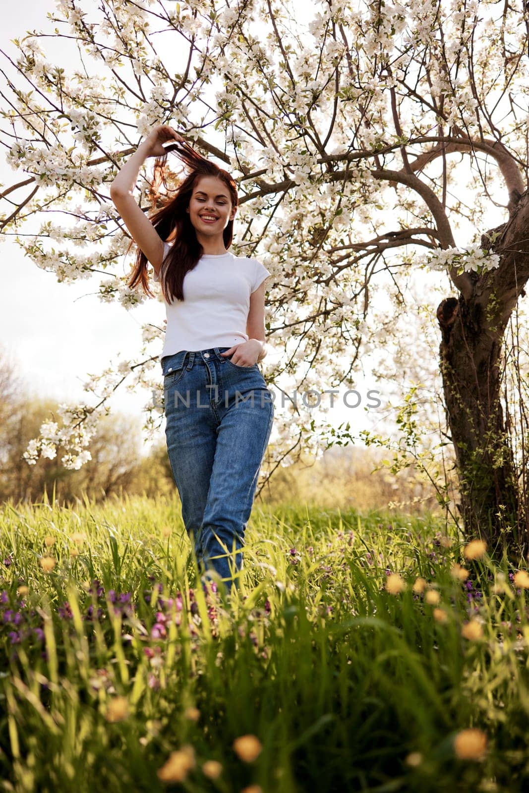 cheerful woman in casual clothes walks in nature near a flowering tree by Vichizh