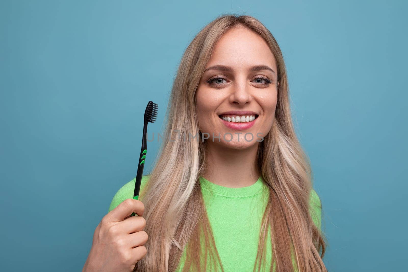 young blond woman with healthy teeth holding a toothbrush on a blue background.