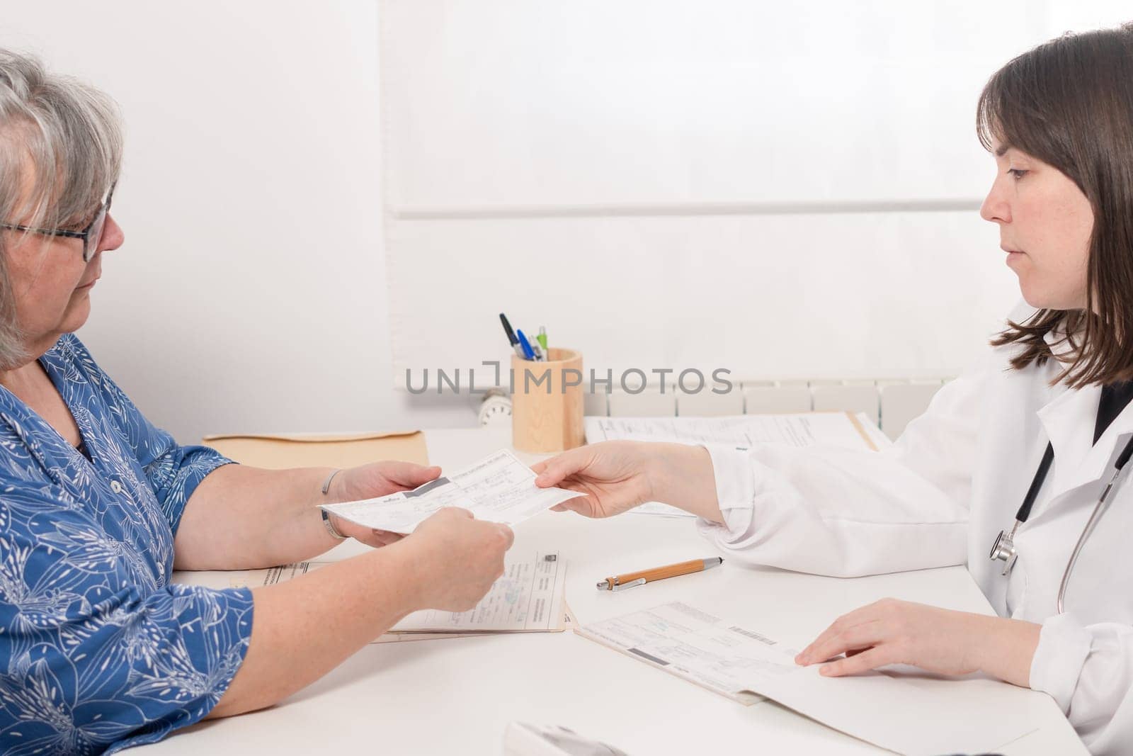 young female doctor handing a prescription to her elderly patient in the doctor's office
