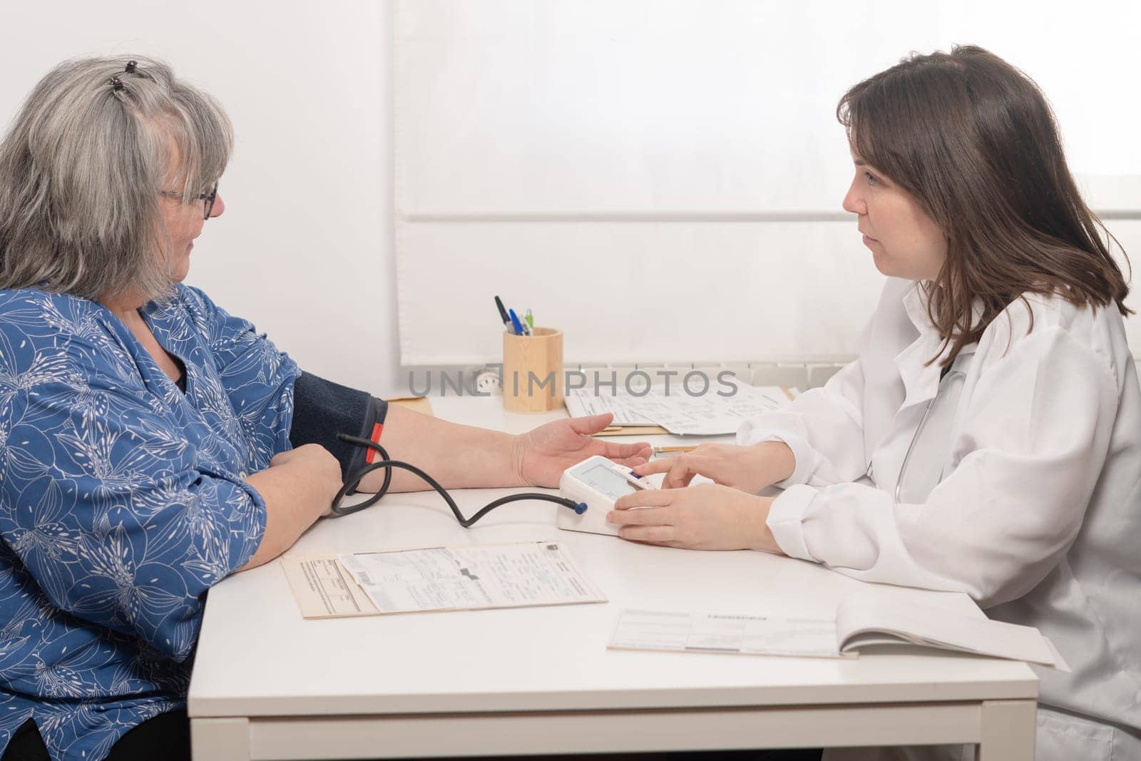 young doctor taking her elderly patient's blood pressure at the office