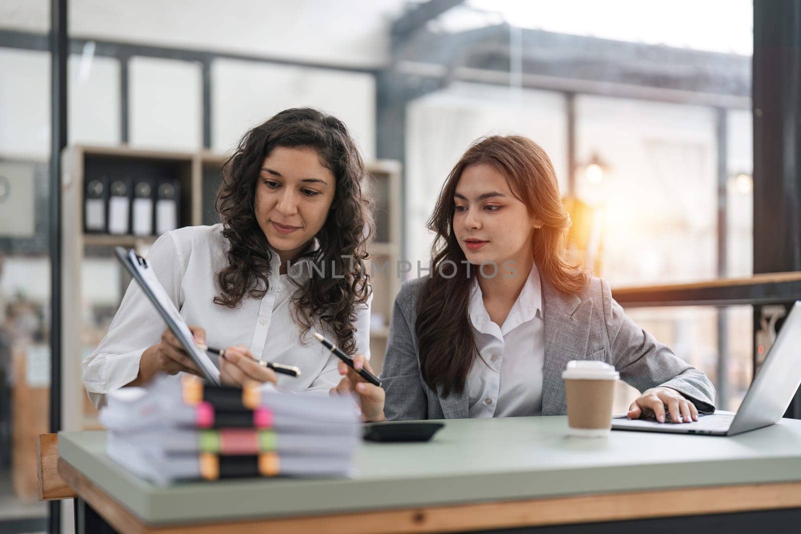 Two smart multiethnic business people working together with laptop while working on project in office.