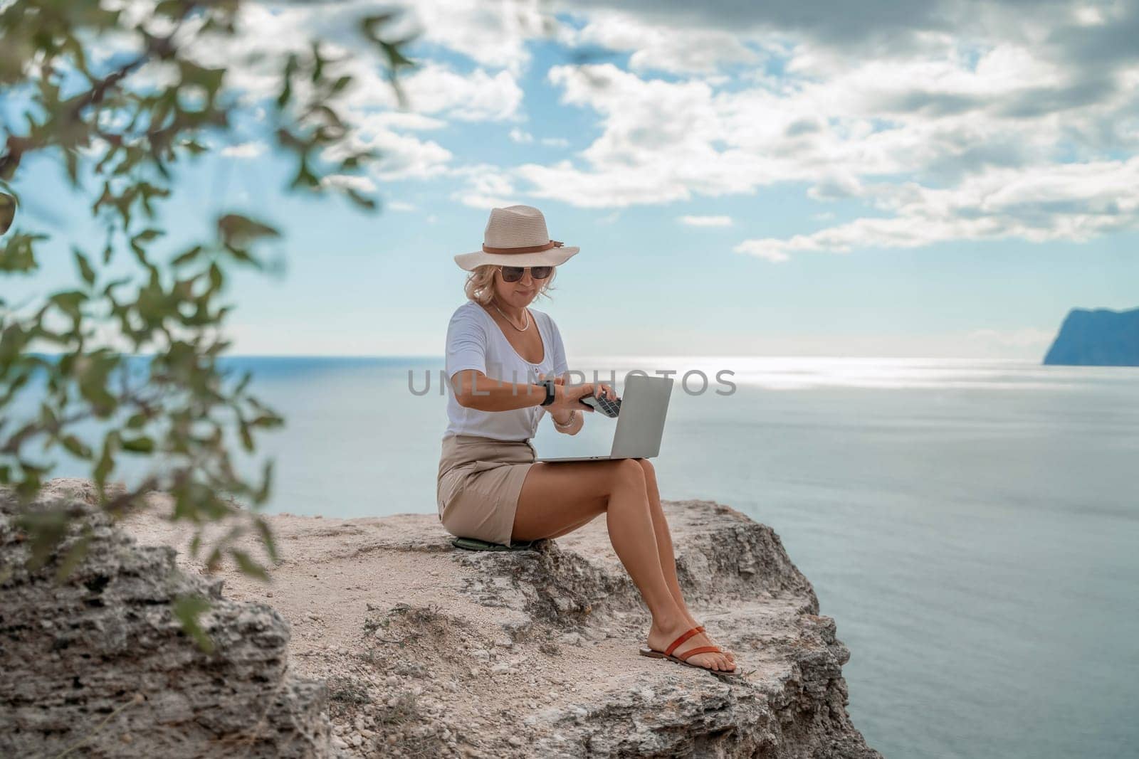 Freelance women sea working on the computer. Good looking middle aged woman typing on a laptop keyboard outdoors with a beautiful sea view. The concept of remote work