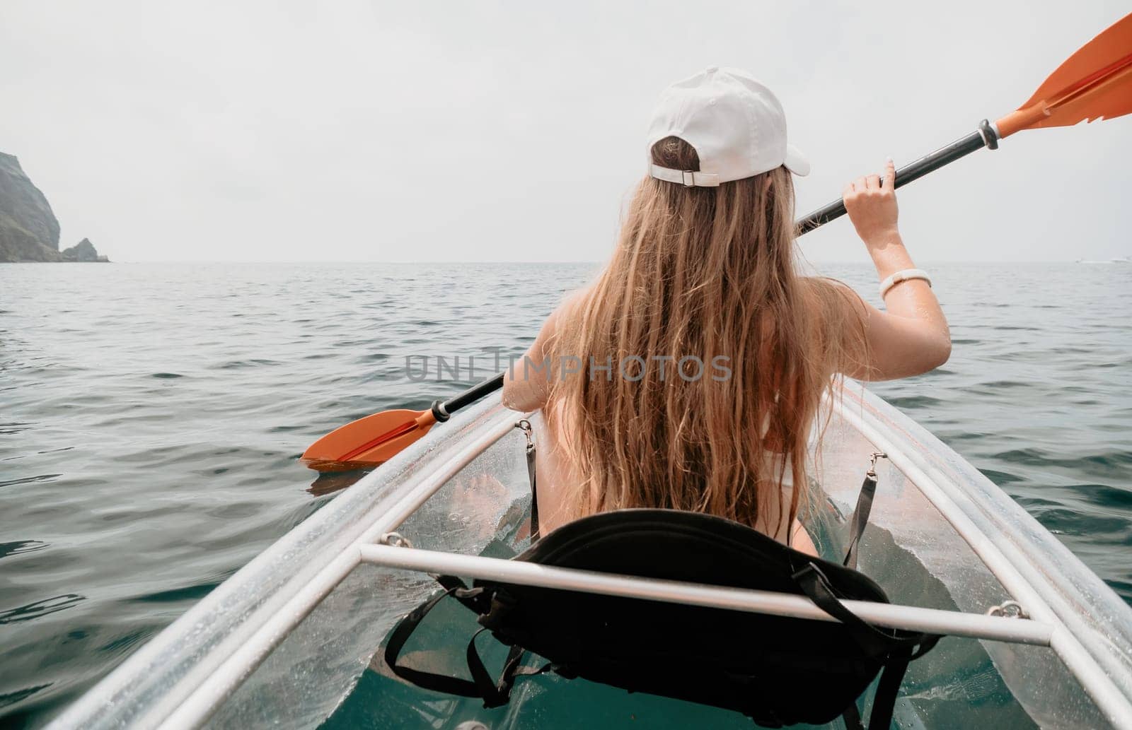 Woman in kayak back view. Happy young woman with long hair floating in transparent kayak on the crystal clear sea. Summer holiday vacation and cheerful female people having fun on the boat.