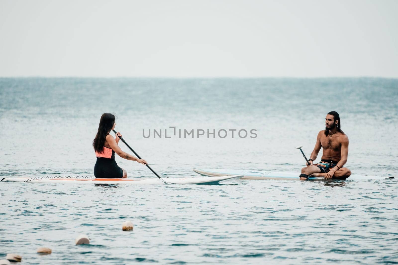 Sea woman and man on sup. Silhouette of happy young woman and man, surfing on SUP board, confident paddling through water surface. Idyllic sunset. Active lifestyle at sea or river