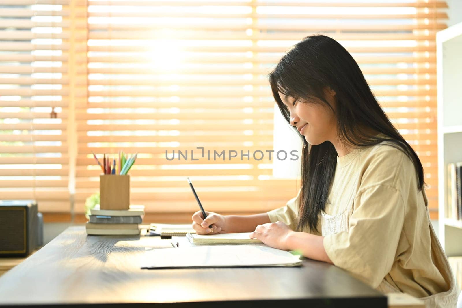 Smiling asian teen girl making notes, ding essay homework assignment at home. Learning and education concept by prathanchorruangsak
