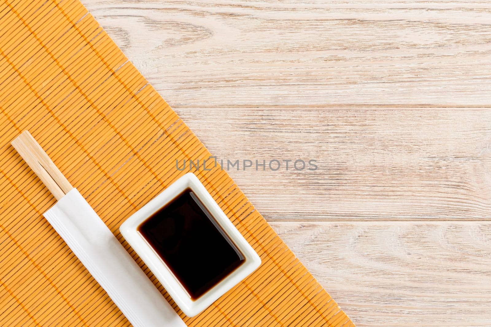 Bamboo mat and soy sauce with sushi chopsticks on wooden table. Top view with copy space background for sushi. Flat lay.