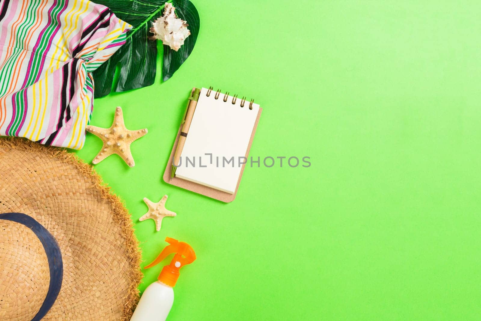 Summer accessories with t-shirt, seashells, flip flops sunscreen bottle and straw hat on green background top view flat lay.