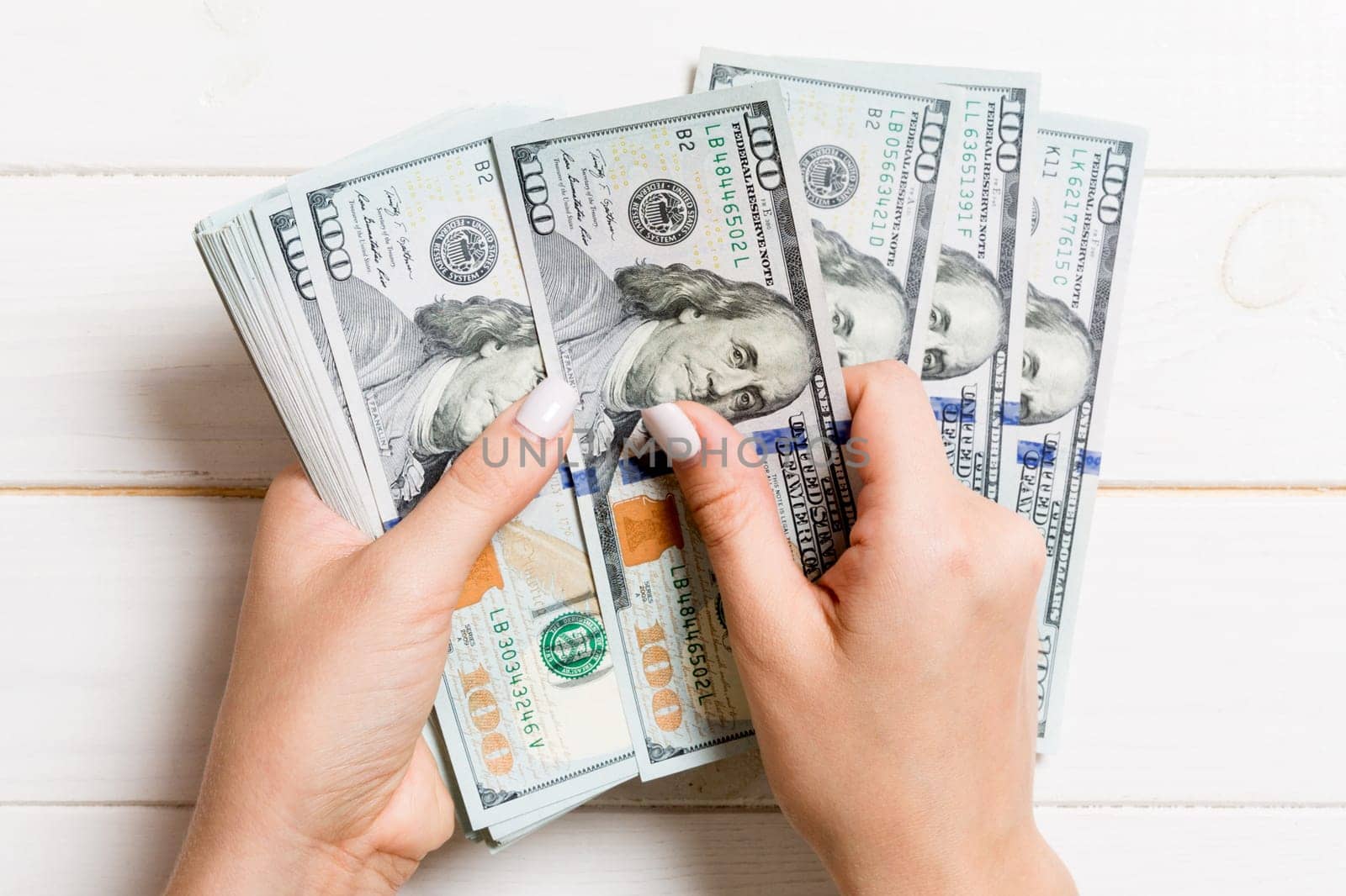 Top view of female hands counting money. One hundred dollar banknotes on wooden background. Business concept.