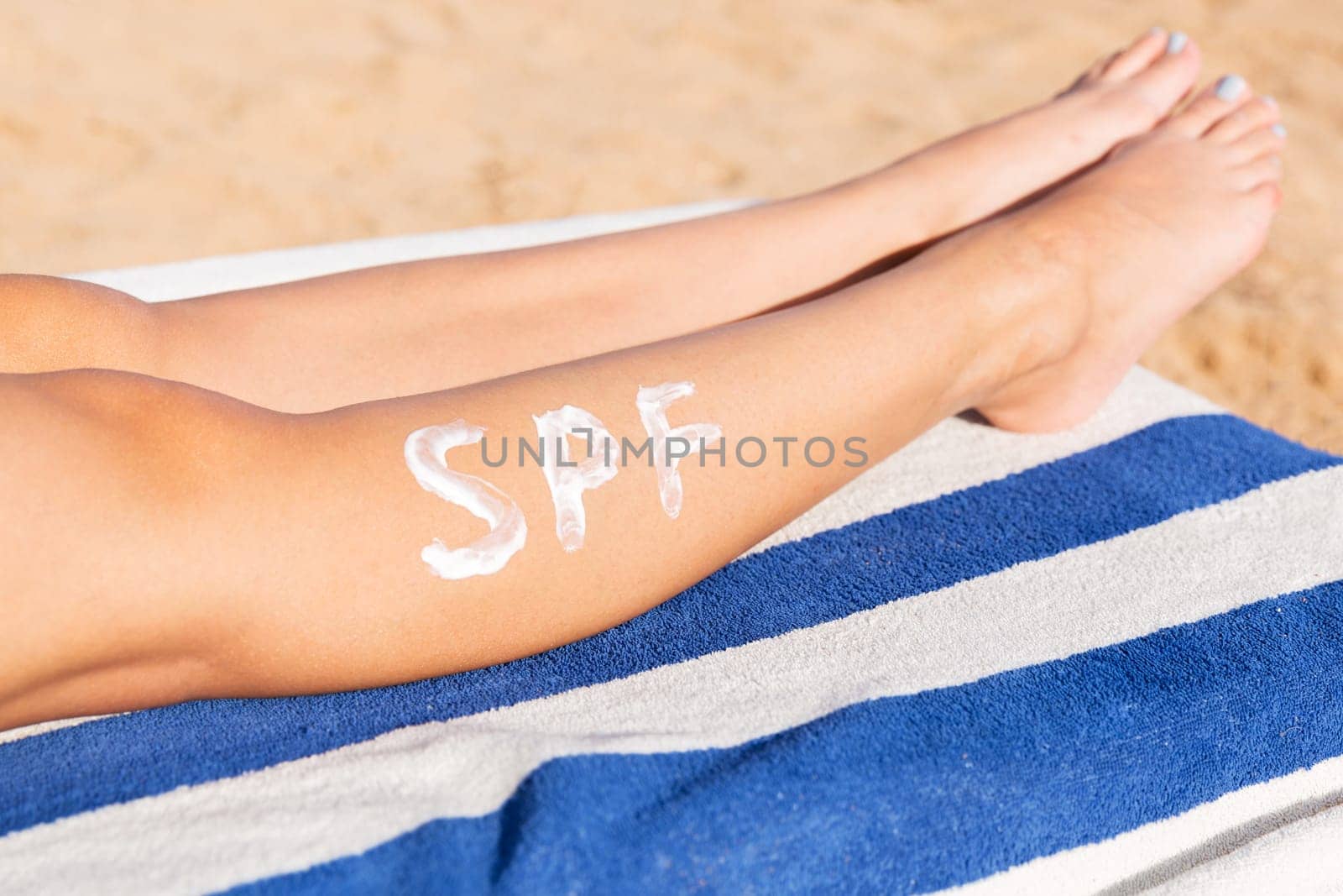 Female legs with spf word made of sun cream at the beach. Sun protection factor concept.