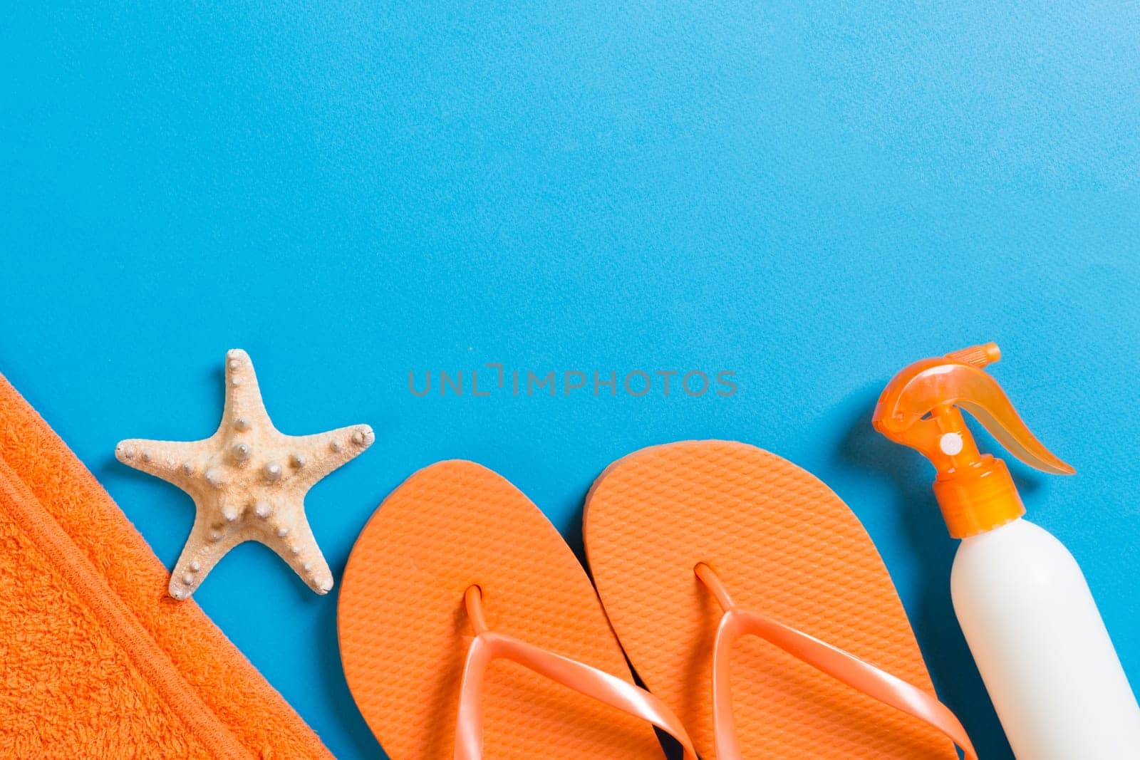 Top view of Beach flat lay accessories. sunscreen bottle with seashells, starfish, towel and flip-flop on Colored background with copy space.