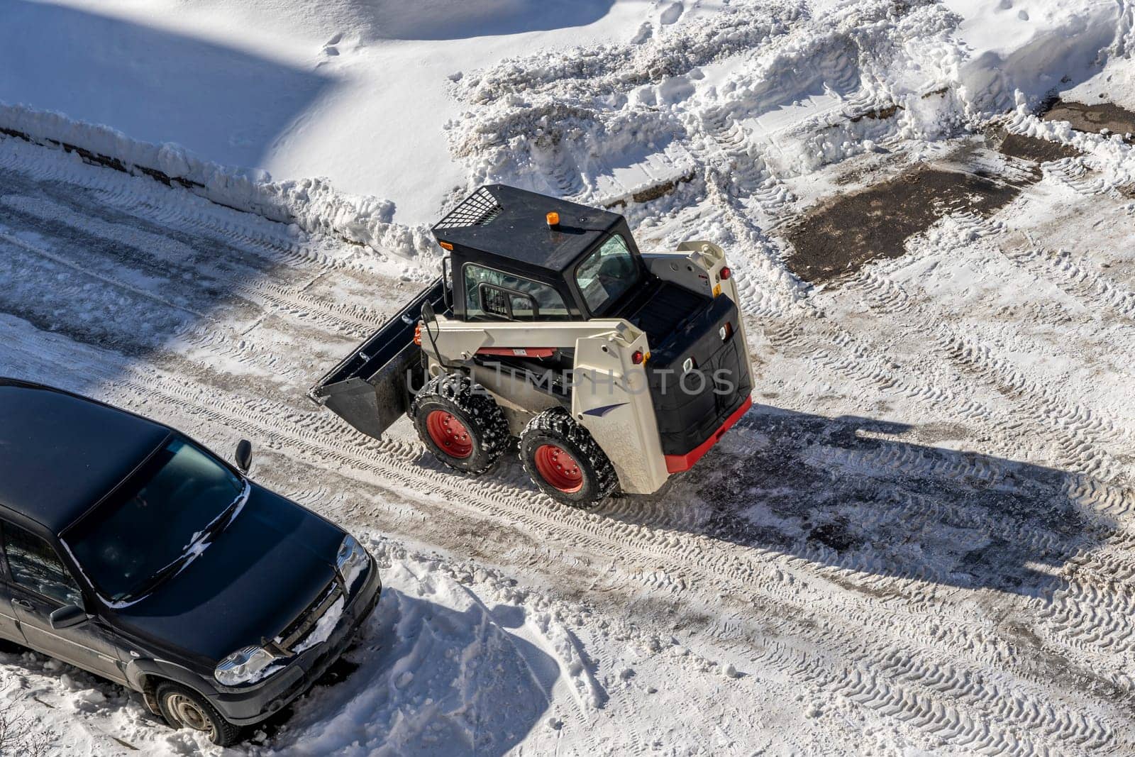 a small snowplow with a bucket cleans yard roads from snow. Maintenance of the territory. city snow cleaning service department at work