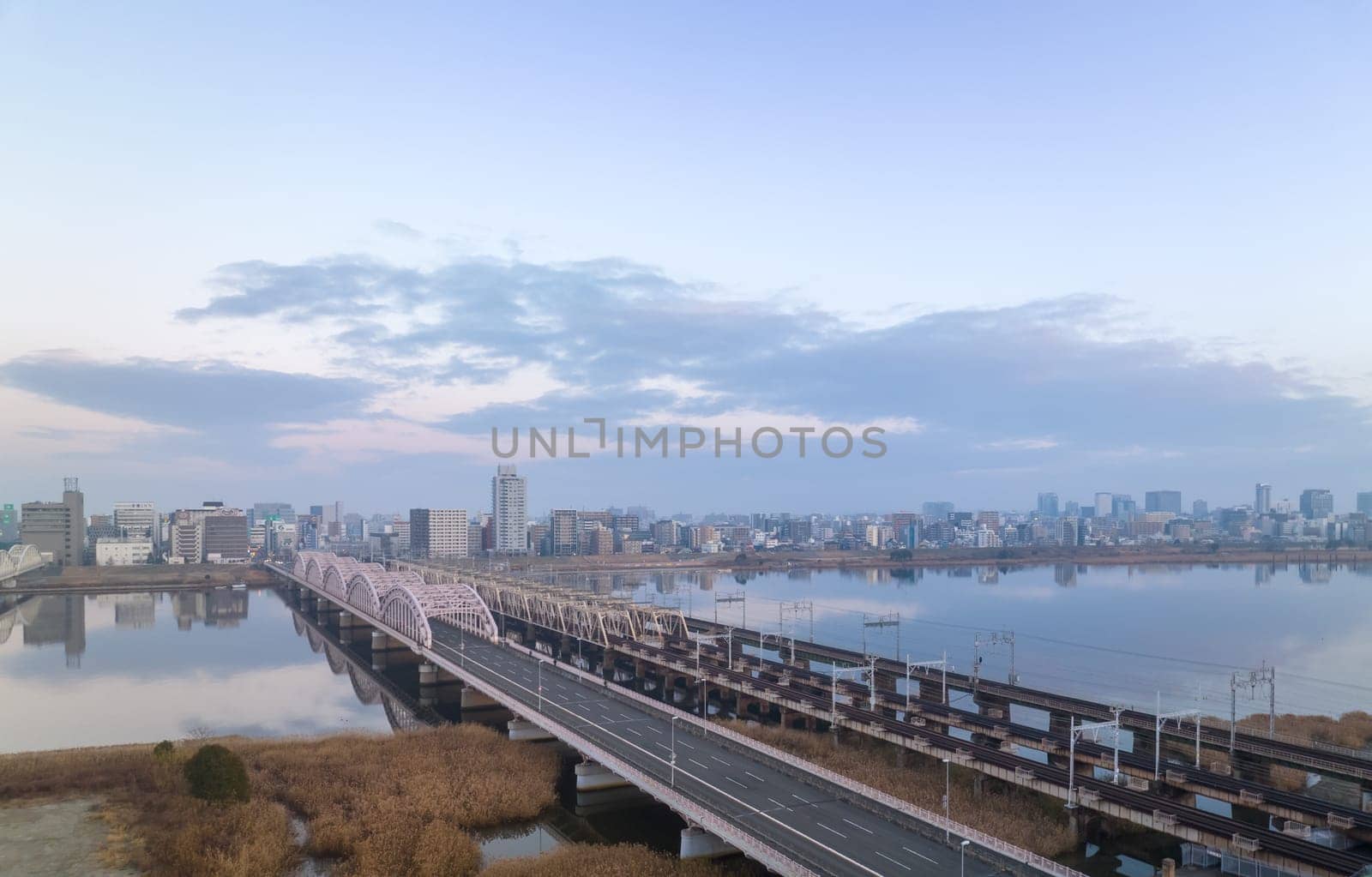 Empty vehicle and railroad bridges over river by city at dawn by Osaze