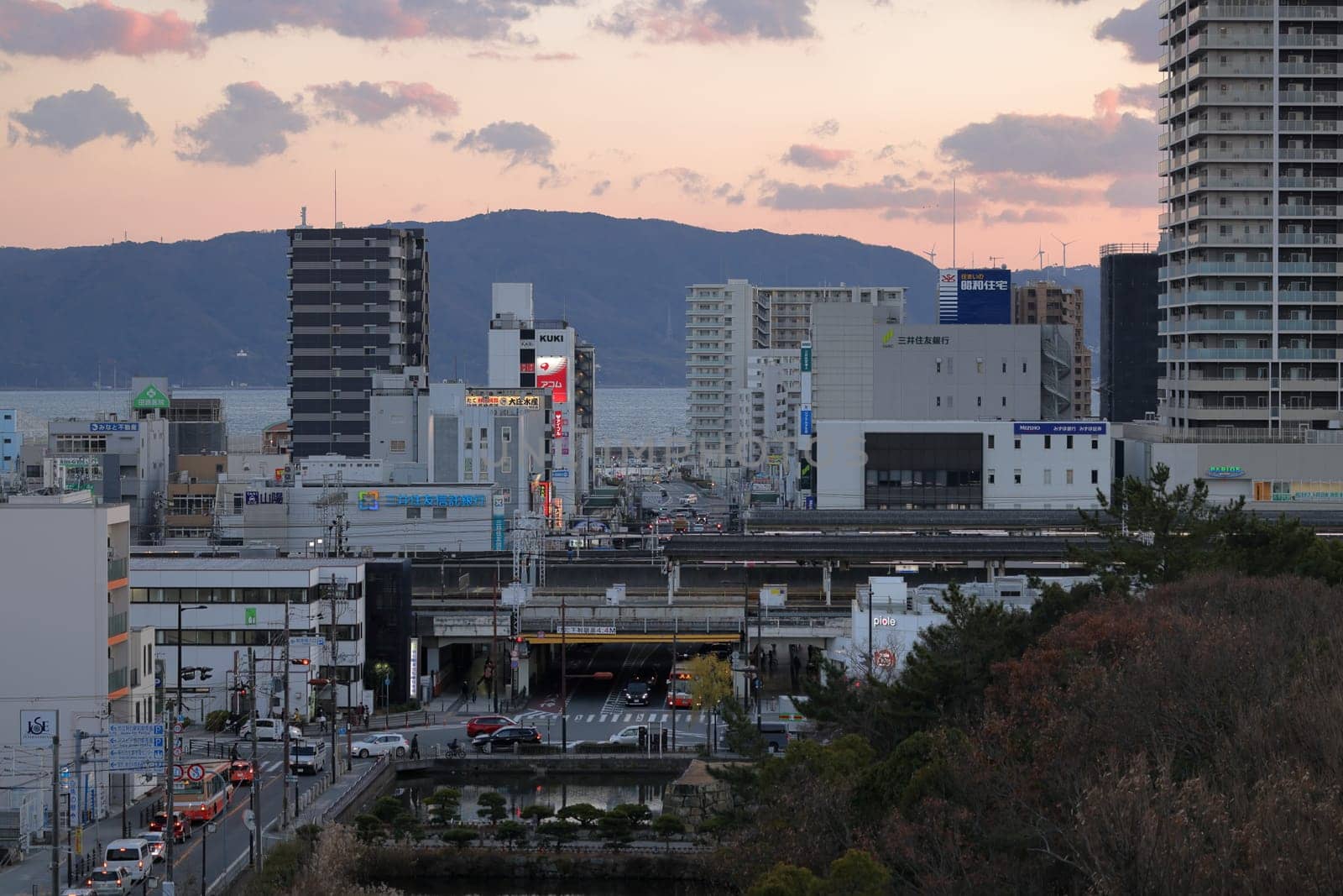 Akashi, Japan - December 29, 2022: Sunset over traffic in intersection under elevated train tracks in small town by Osaze