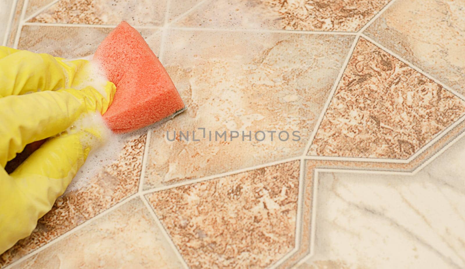 Man hand in yellow glove with red sponge in washing solution on kitchen floor.Washing floors by the washing solution.