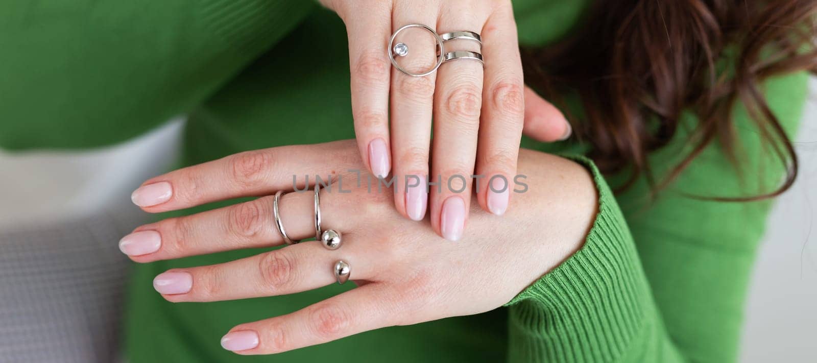 Female hands with trendy light pink manicure wear stylish jewerly. Silver rings and bracelet set with feminine wristwatch