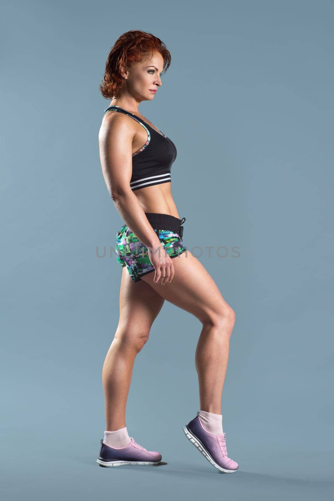 Mature athletic redhead woman doing fitness exercises, gray studio background by VH-studio