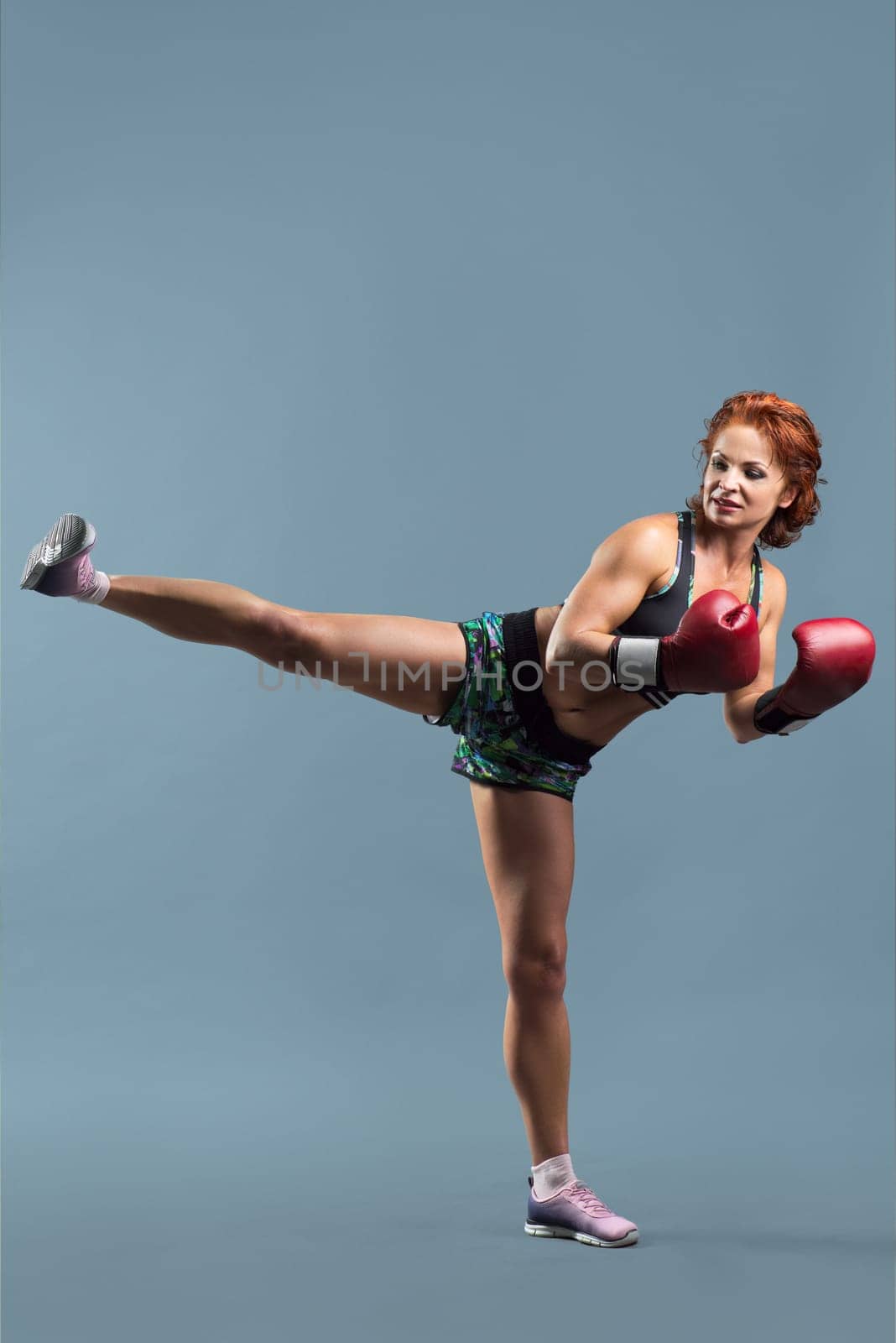 Mature woman in sportswear doing fitness exercises in boxing gloves by VH-studio