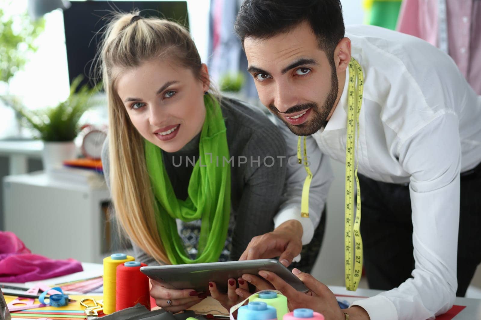 Woman and man stylist designers are holding tablet and discussing new clothes sketch by kuprevich