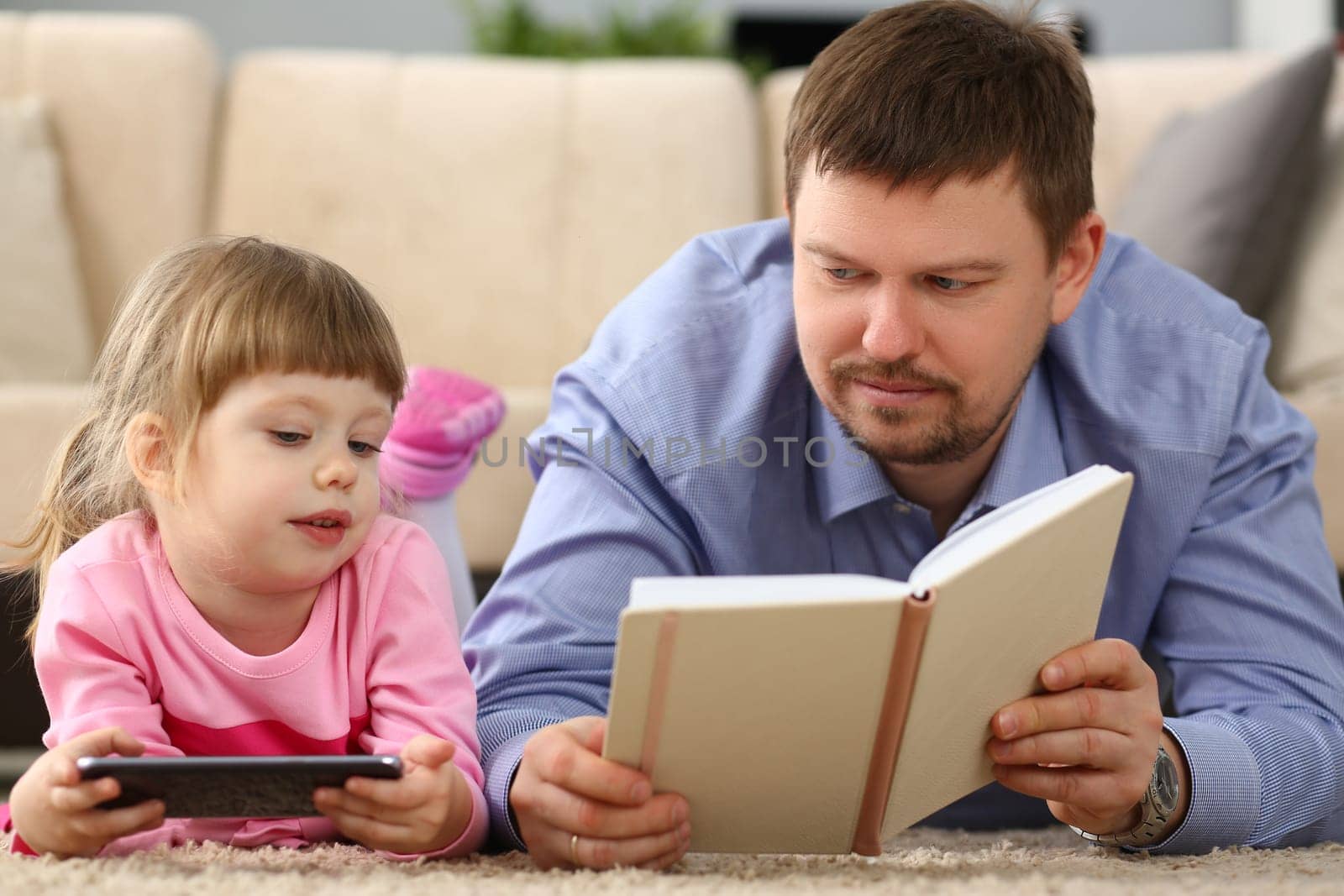 Dad reads a book to daughter holding smartphone lying on floor by kuprevich