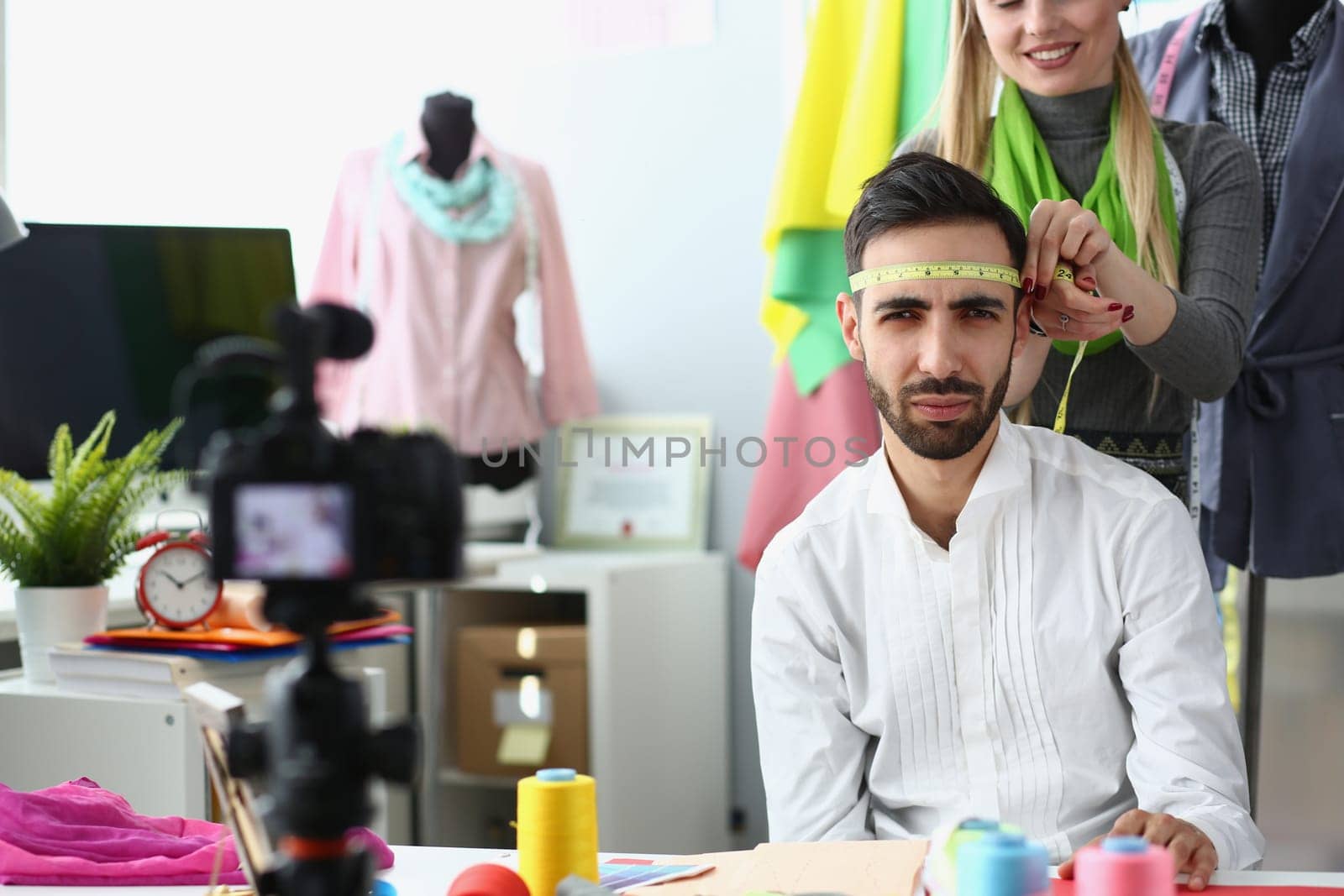 Woman seamstress stylist jokes and measures head of a male designer with centimeter. by kuprevich
