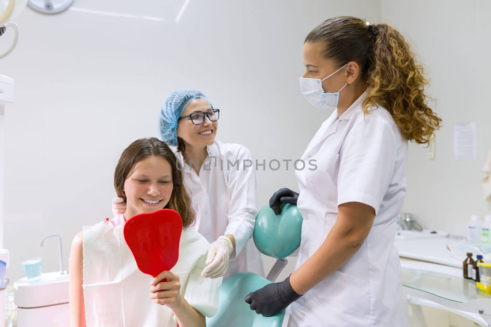 Teenager girl in dental chair with mirror looking at her teeth by VH-studio