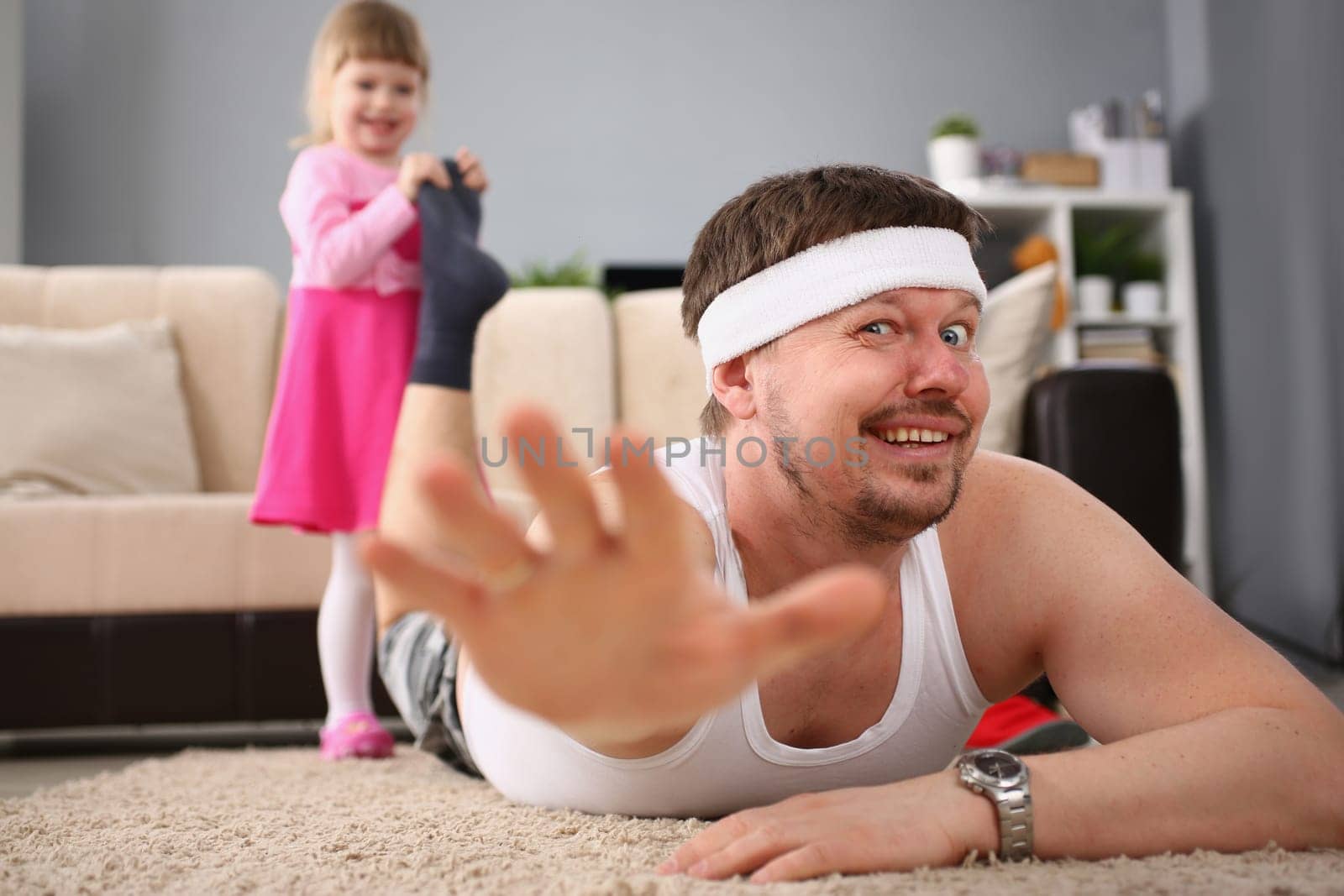 Laughing little girl pulling dad leg on floor. Games with young children at home and family leisure