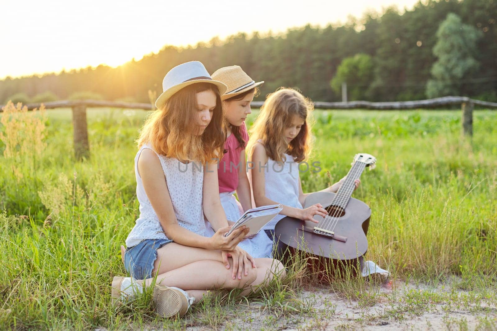 Girls with classical guitar on nature. Children relaxing on lawn, learning to play the guitar, singing songs, sunset on summer meadow background