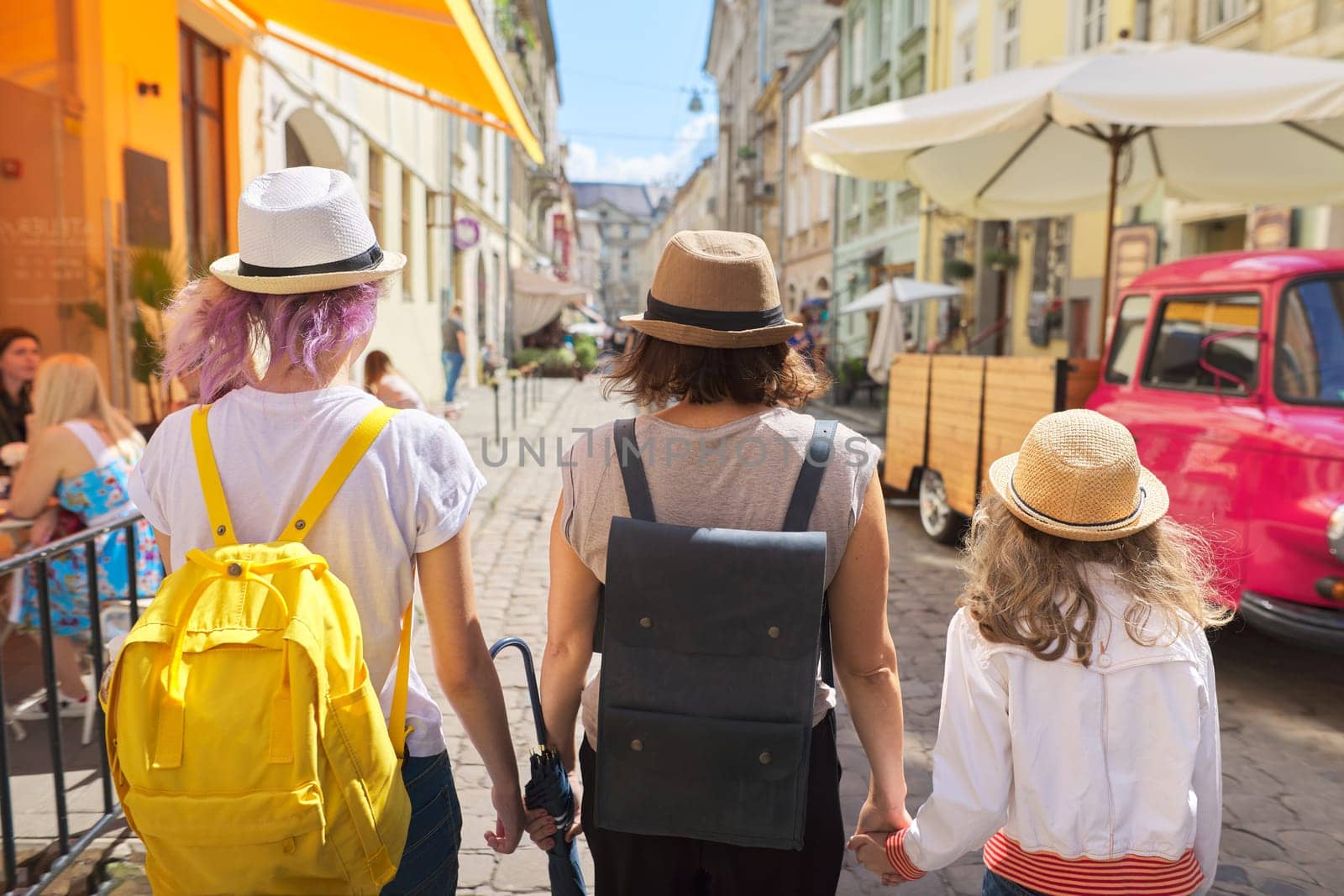 Mother and two daughters walking in old tourist city, back view by VH-studio