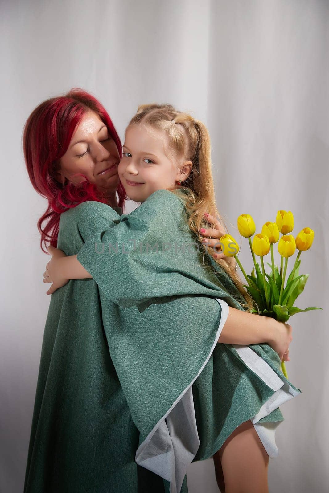 Amazing pretty mother and daughter having fun with flowers in 8 March or in Mother's day. Red haired mom and small little blonde girl having lovely free time on white background in studio