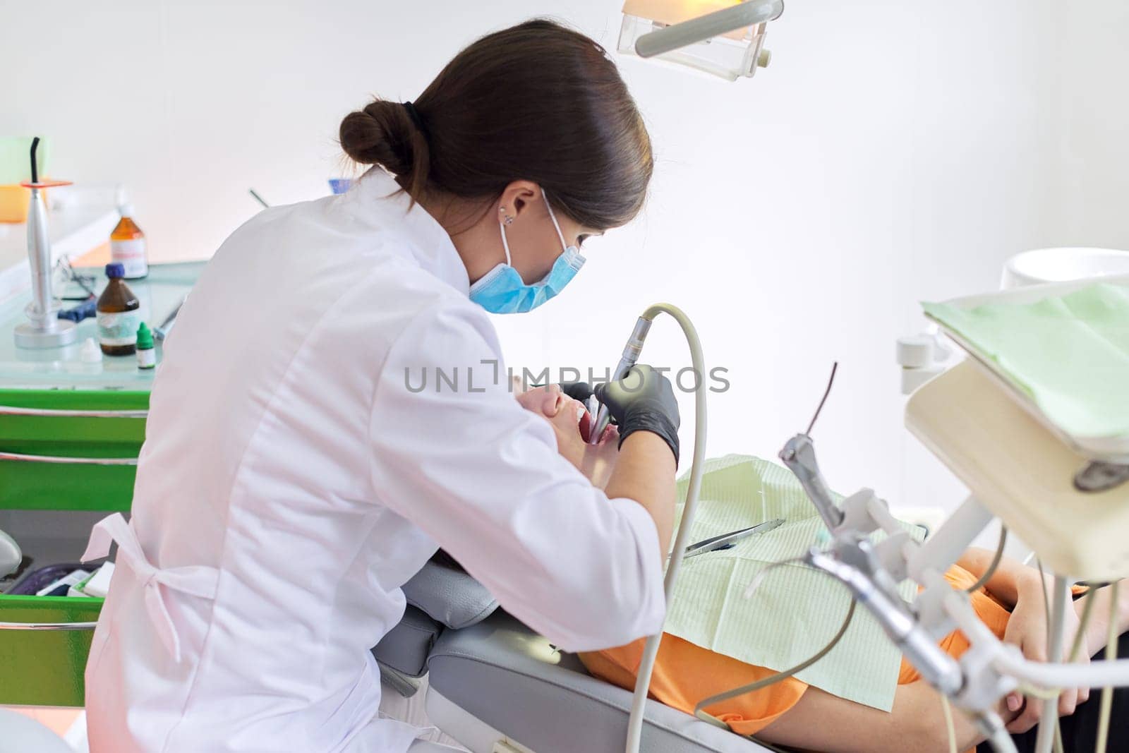 Woman doctor dentist treating teeth to girl patient in dental office by VH-studio