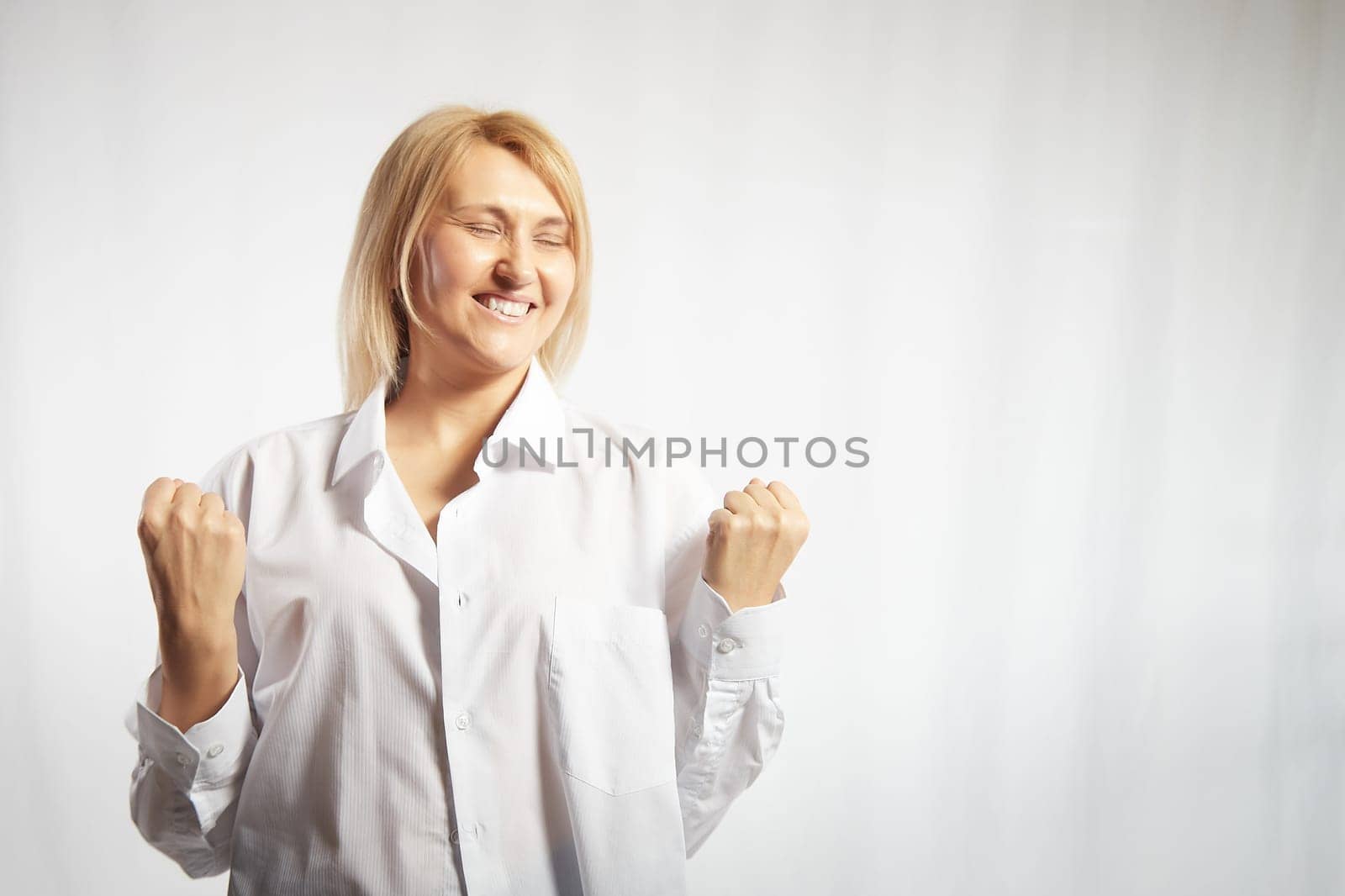 Portrait of a pretty blonde smiling woman posing on white background. Happy girl model in white shirt in studio. Lady winner is joyfull. Copy space