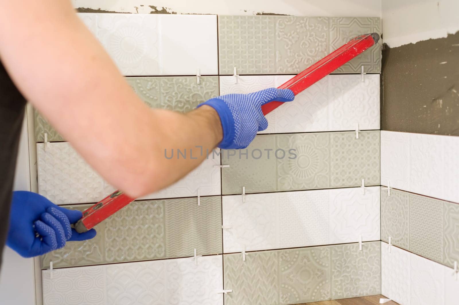 Male worker glues tiles on kitchen wall, uses level and professional materials and tools. Renovation, repair, construction
