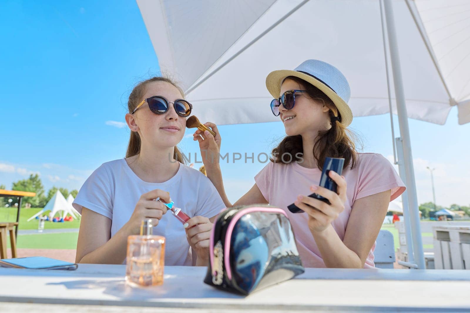 Two teenage girls making make-up, sitting in summer outdoor cafe. Youth, teens, communication, people concept