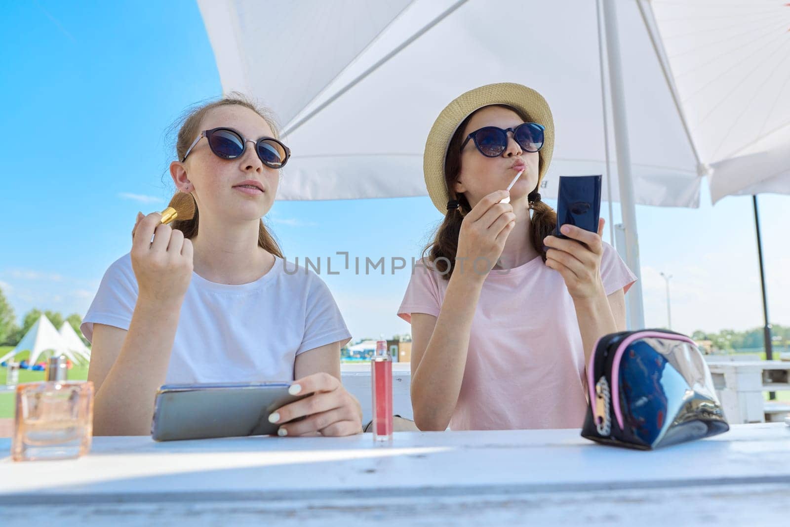 Two teenage girls making make-up, sitting in summer outdoor cafe. Youth, teens, communication, people concept